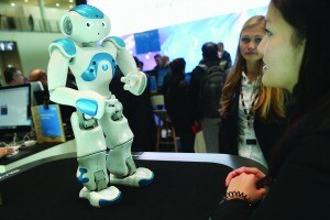 HANOVER, GERMANY - MARCH 14: A stand hostess talks to a NAO Watson robot at the IBM stand at the 2016 CeBIT digital technology trade fair on the fair's opening day on March 14, 2016 in Hanover, Germany. The 2016 CeBIT will run from March 14-18. (Photo by Sean Gallup/Getty Images)