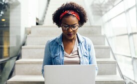 Focused young African female college student working on a laptop on some stairs on campus preparing for an exam