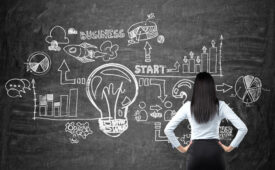 Full length rear view of brunette woman in formal clothes who is looking at the business flowchart on the black chalk board. The concept of business ideas development.