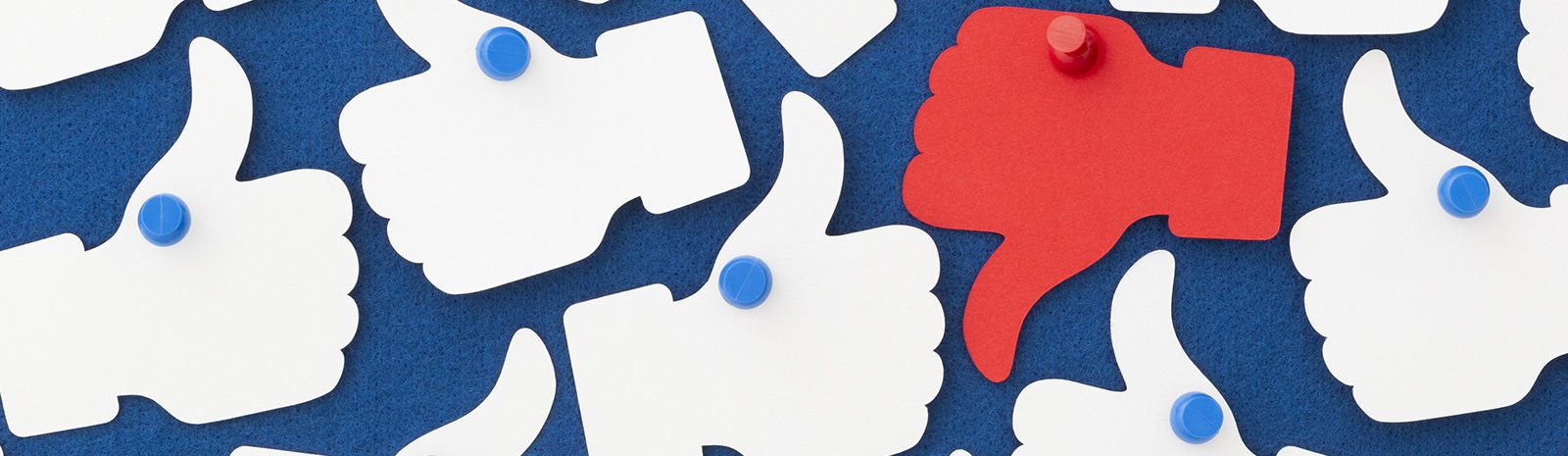 One red thumbs down amongst many white thumbs up pinned to a notice board. Alternative viewpoint, opinion, social media etc.