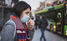 Side view of woman wear face mask and coughing while standing in the town, looking down