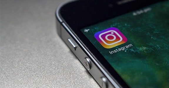 Foto onde um celular está sendo exibido em close, apenas o seu canto superior esquerdo. Icone do Instagram aparece na tela