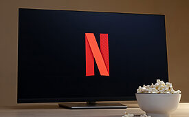 Tela de TV exibe logo Netflix com tigela de pipoca ao lado.