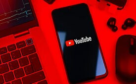 Smartphone com logo do YouTube, laptop e mouse em ambiente vermelho.