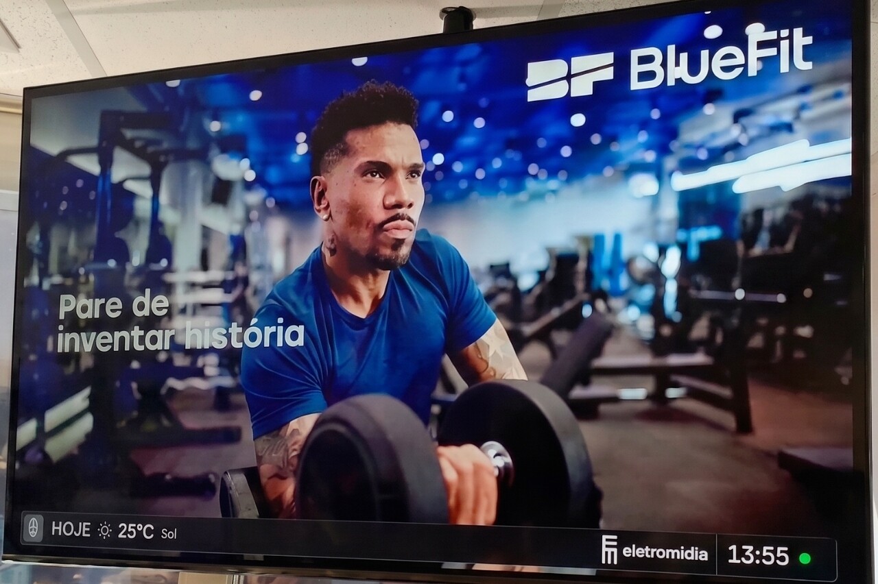 Tela de televisão mostrando anúncio da BlueFit com atleta e haltere.