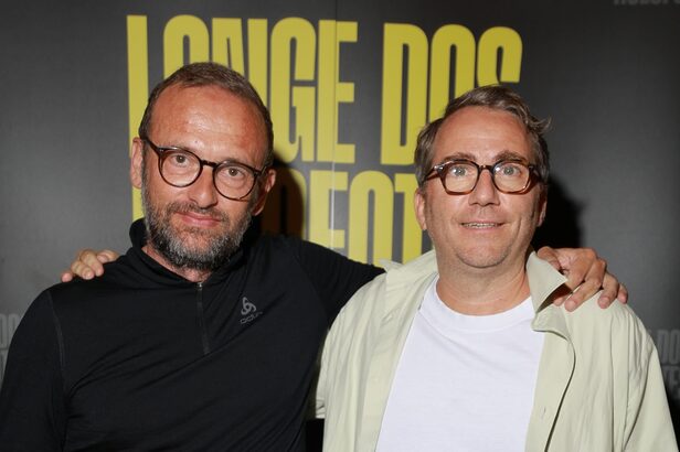 Dois homens de óculos sorrindo, um com barba e o outro liso, em evento.