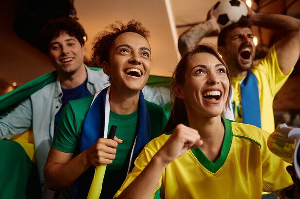 Torcedores brasileiros vibrando com alegria, vestindo camisas amarela e verde, assistindo a um jogo.