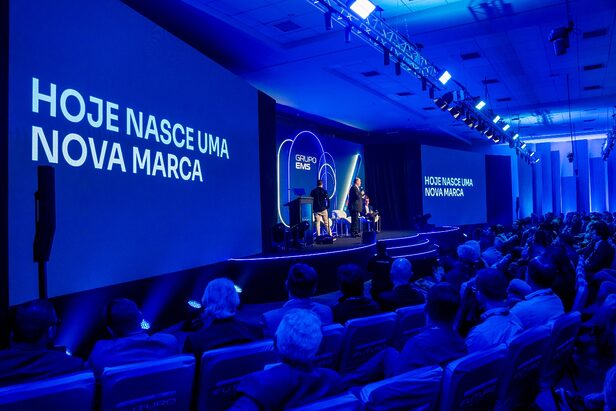 Lançamento de nova marca 'GRUPO EMS' em auditório, com apresentadores e plateia assistindo em evento.
