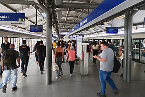 Vista da plataforma de metrô com passageiros caminhando e esperando, portas do trem fechadas.