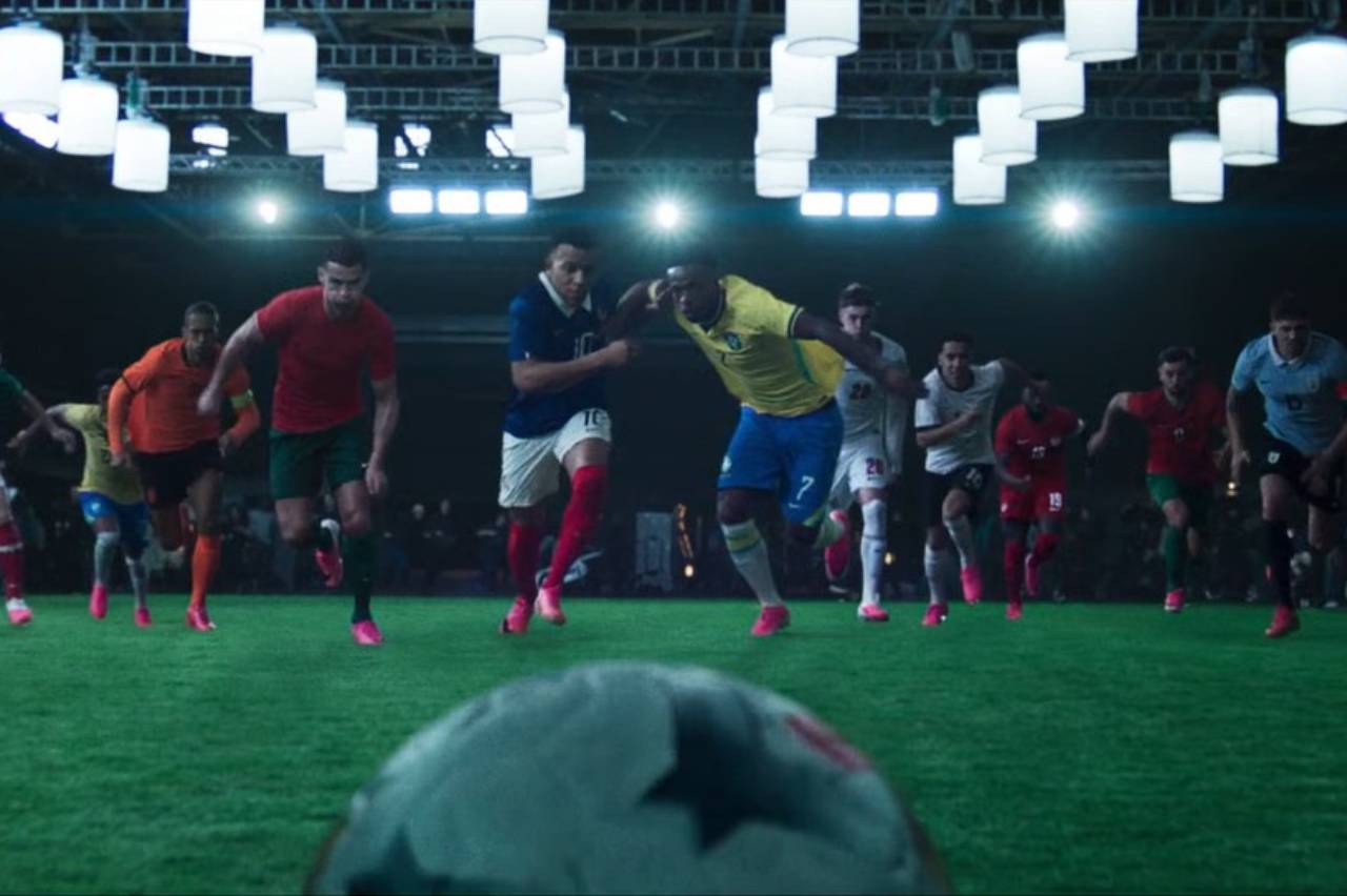 Jogadores de futebol de seleções (Portugal, França, Brasil) em campo iluminado, bola em destaque, em plena corrida.