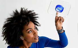 Mulher negra com cabelo crespo tocando um botão "Shop" virtual flutuante em interface digital.