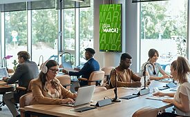 Pessoas trabalhando em laptops em escritório moderno; tela exibe "SUA MARCA" em verde.
