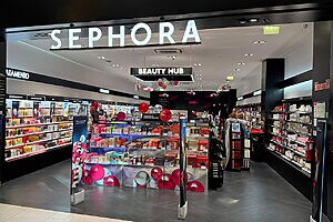 Entrada da loja Sephora com letreiro luminoso, prateleiras de maquiagem e produtos de beleza à mostra.
