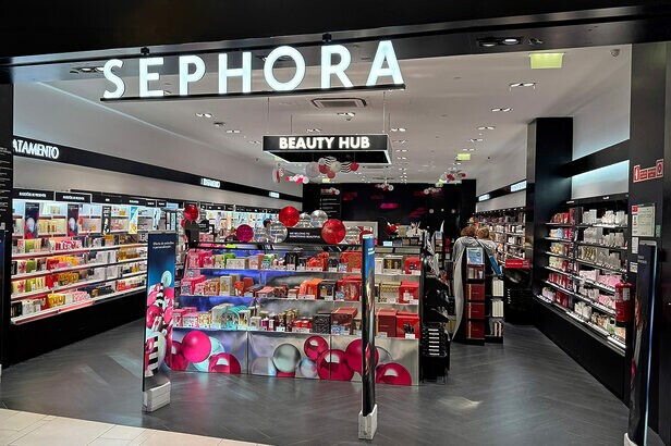 Entrada da loja Sephora com letreiro luminoso, prateleiras de maquiagem e produtos de beleza à mostra.
