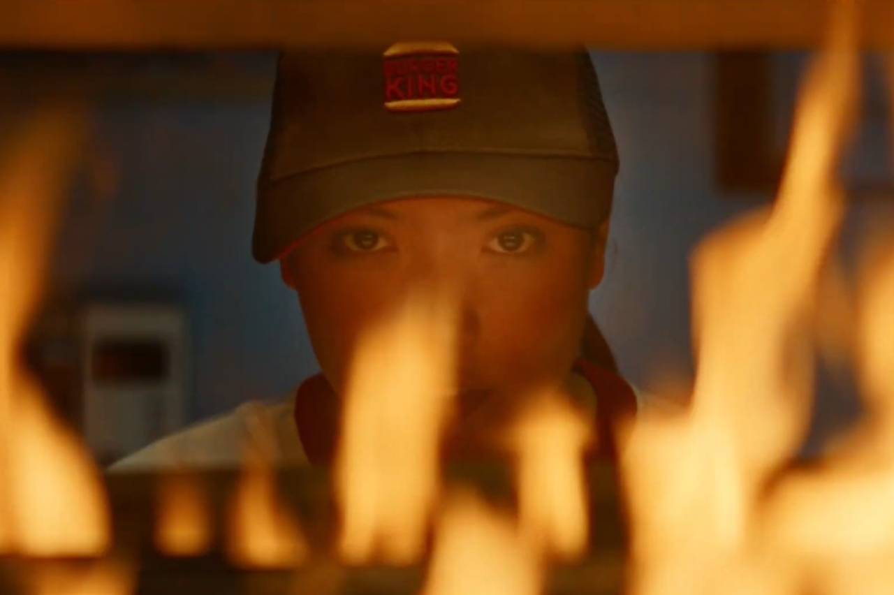 Campanha Burger King - Rosto de mulher com boné e olhos fixos, encoberto parcialmente por labaredas alaranjadas.