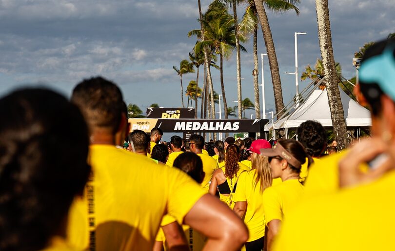Multidão de corredores com camisas amarelas se aproxima da área de medalhas em evento esportivo.