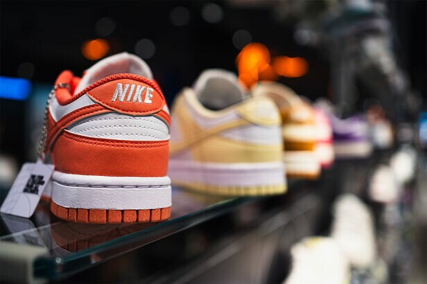 Tênis Nike Dunk laranja e branco em prateleira de loja, outros tênis coloridos desfocados ao fundo.