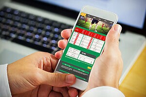 Mãos seguram smartphone com aplicativo de apostas esportivas, exibindo jogos de futebol e odds.