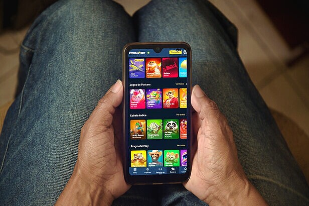 Pessoa segurando smartphone com aplicativo de jogos de cassino ou apostas, vestindo jeans.