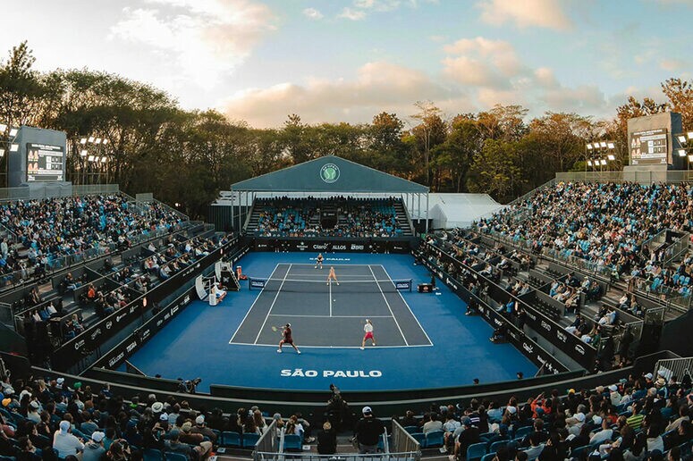 Torneio de tênis em São Paulo: quadra azul iluminada, jogadores em ação e arquibancadas lotadas.
