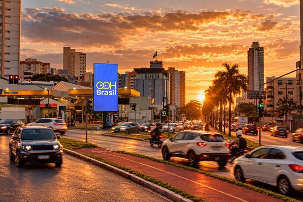 Rua urbana movimentada com carros e ciclovia ao pôr do sol, prédios altos e painel digital OOH Brasil.