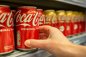 Mão humana pegando uma lata de Coca-Cola na gôndola