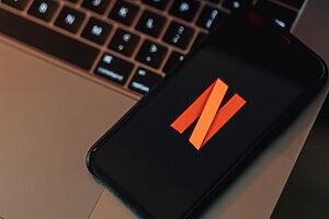 Smartphone preto com logo Netflix em tela, sobre teclado de notebook prateado.